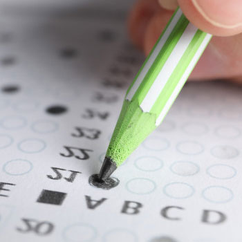 Close up image of a green pencil shading the letter a on an exam paper