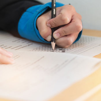 A close up image of a student using a pen to write answers on a GRE test